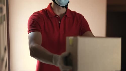 An young mailman courier with a protective mask and gloves is delivering a parcel directly to a cu
