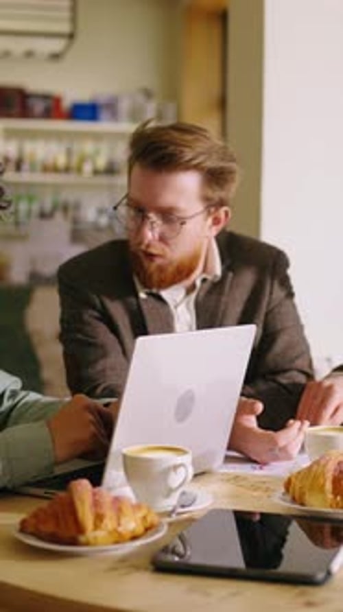 Young Creative Colleagues Collaborating on Laptop in Cozy Cafe Setting During Informal Business