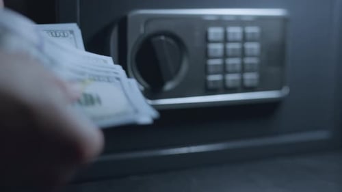 A Businessman is Counting Money with a Safe on Background