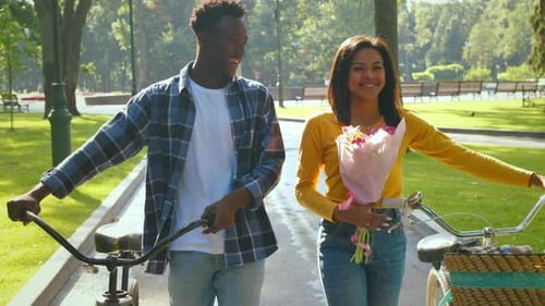 Young Couple Enjoys Biking Together in a Sunny Park with Flowers