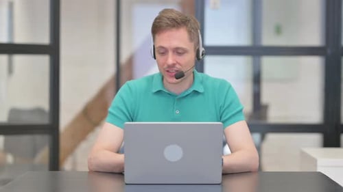 Mature Adult Man with Headset Talking for Video Chat on Laptop in Call Center