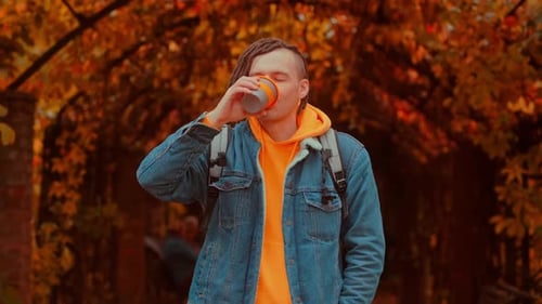 Young Adult Drinks Coffee in Autumn Park