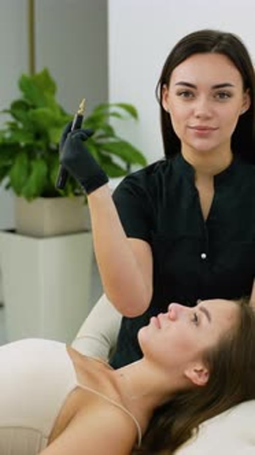 Beautician Holding Microblading Tool With Client Lying Down