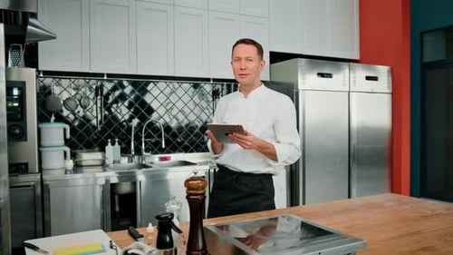 Professional chef using tablet computer for recipes while working in modern kitchen cooking concept