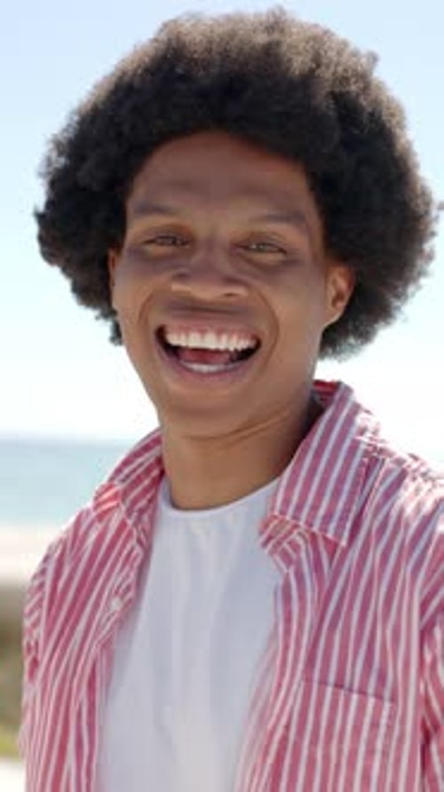 Vertical video: Smiling man enjoying sunny day at beach, wearing striped shirt