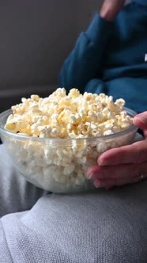 Mann isst Popcorn in der Glasschale auf dem Sofa