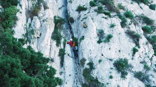 Young fit male rock climber fully equipped and wearing protective helmet climbing on cliff
