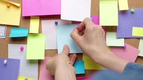 A woman's hand pins a blank paper note on a cork board. Post reminder. A place to write an idea.
