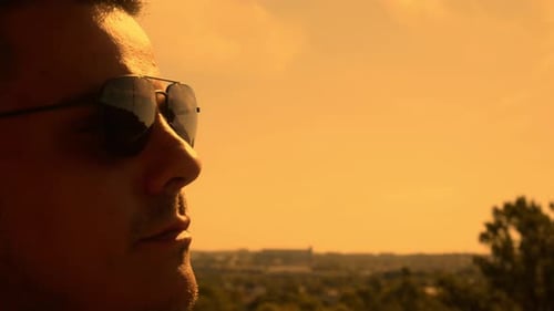 Man Puts on Sunglasses Overlooking City at Sunrise
