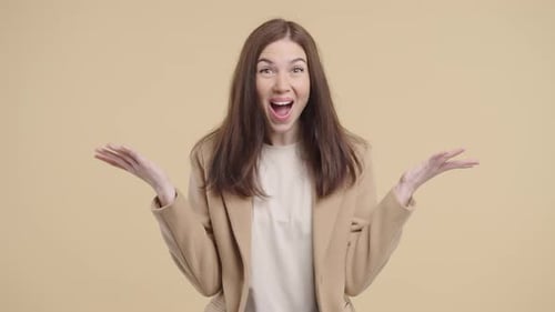 Excited woman gestures in front of neutral background