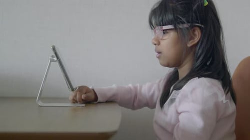 A Young Child Completely Engrossed in Her Tablet Screen While Sitting at the Table