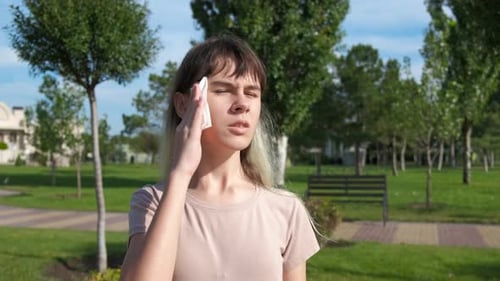Woman Wipes Sweat in City Park on Sunny Day