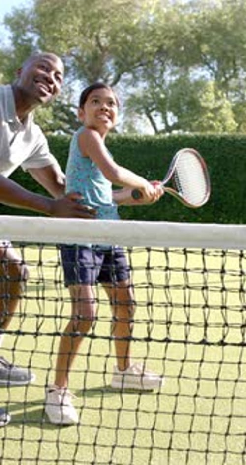 Vertical video: Teaching tennis, father guiding daughter on court, holding racket together