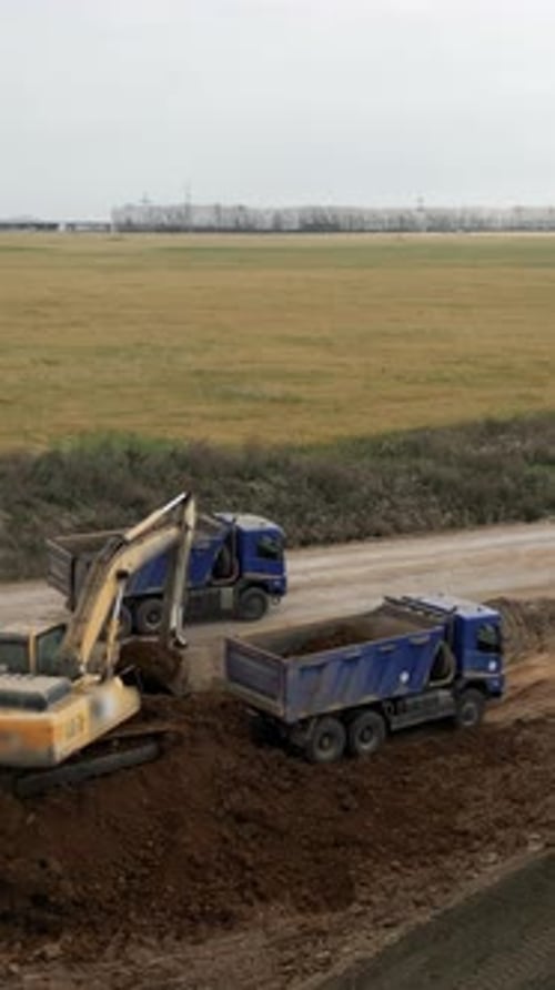 Excavator Filling Trucks with Dirt in Rural Setting