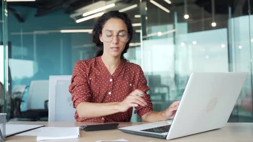Busy young businesswoman making financial calculations using laptop computer taking notes sitting