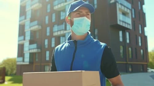 Delivery Man Holding Cardboard Box at Street Wear Protective Medical Face Mask and Gloves Quarantine