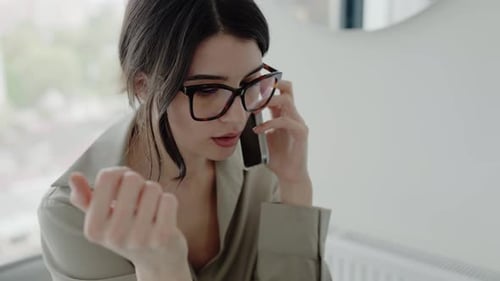 Young Woman with Glasses Talking on Phone at Home Office