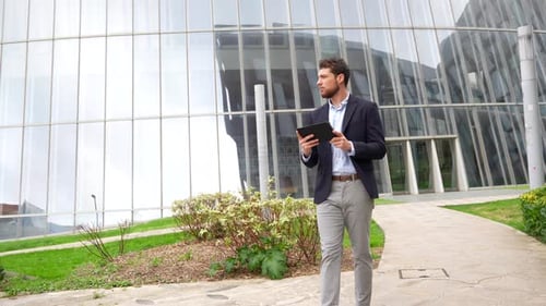 Young male businessman or entrepreneur outside the office, walking with a tablet in his hand