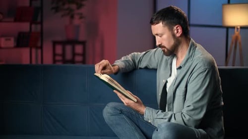 Man Reading a Book on Blue Couch at Home