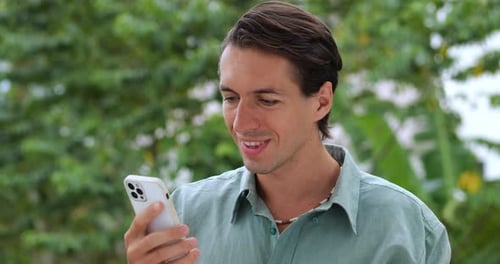 Handsome Caucasian Young Man Using a Smartphone Scrolling Browsing the Web and News Feed Checking