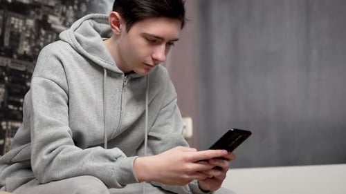 Teen Focused on Smartphone Indoors Wearing Gray Hoodie