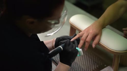 Top View of Beautician Female Wearing Black Gloves Expertly Using Electric Nail Drill to Gently
