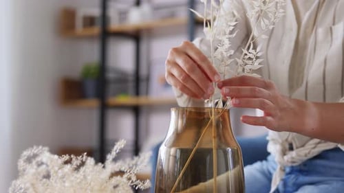 Woman Arranges Dried Flowers in Vase at Home