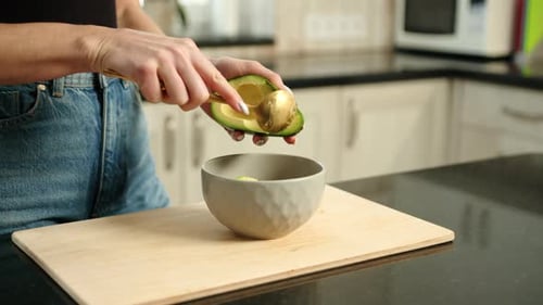 Scooping Avocado into Bowl with Spoon in Kitchen