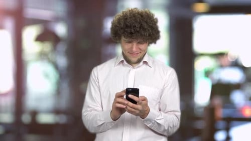 Portrait of a Young Man with Curly Hair Using His Smartphone Indoors