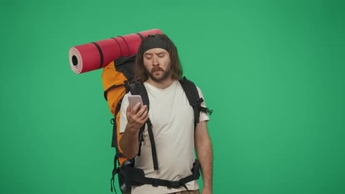 Man Tourist with Backpack Holding Smartphone Searching for Right Direction Isolated on Green