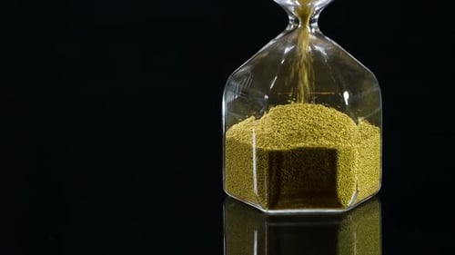 Hourglass with Flowing Gold Beads on Black Background