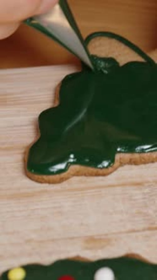 Vertical video. A Woman Carefully Fills a Christmas Tree Cookie with Green Icing, Preparing a Deligh