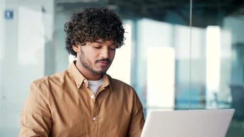 Close up. A young employee using typing on a laptop while sitting at a workplace in a modern office.