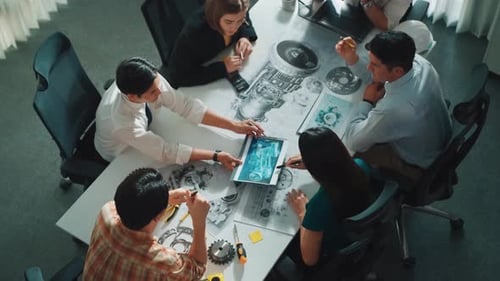 Engineers Collaborate Around a Table with Blueprints and Tablet