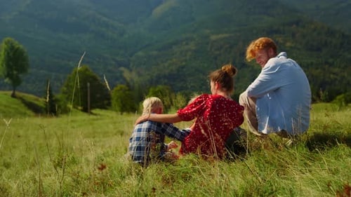 Carefree Happy Family Relaxing On Green Hill. Unrecognizable Parents Enjoying Holiday With Childr...