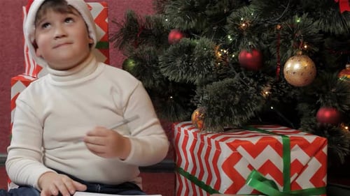 Boy Writes Christmas List By Christmas Tree