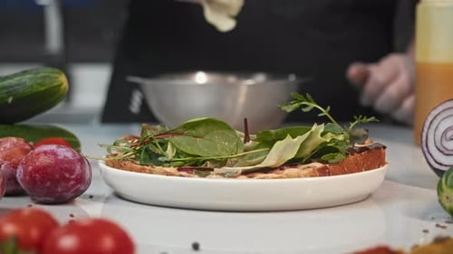 In Restaurant's Kitchen Chef Makes Sandwich with Toasted Bread He Puts Leaves of Green Salad on