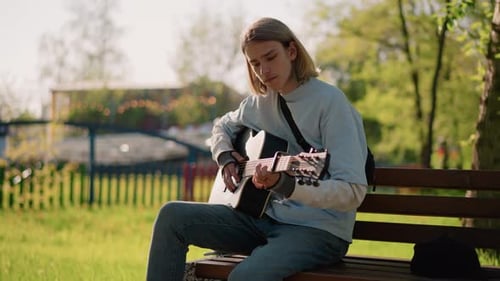 Young Man Playing Guitar on Park Bench