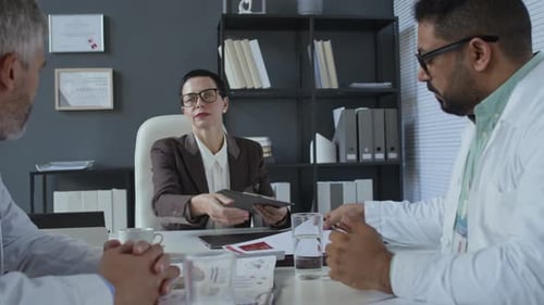 Doctors Reviewing Reports during Office Meeting with Female Director
