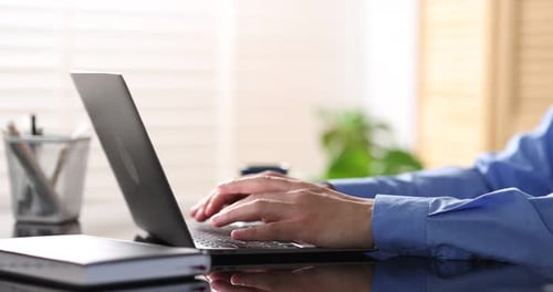 Man with cup of coffee working on laptop at desk in office, closeup