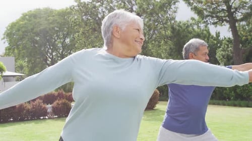 Happy senior diverse couple practicing yoga in garden