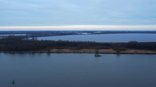 Medium drone shot of a small vessel traveling downstream on the river in south of Netherlands.