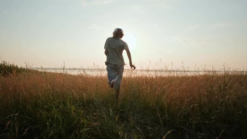 Excited Child Running in Tall Grass toward Lake at Sunset