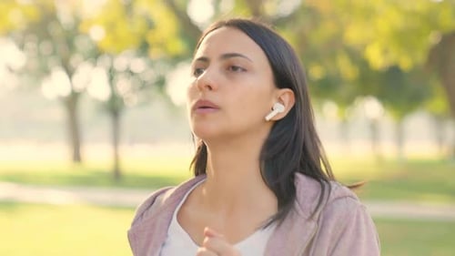 Woman Jogging Through Park with Earbuds