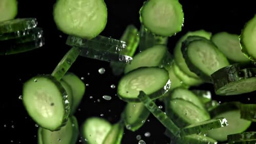Fresh Cucumber Slices Falling Against Dark Background