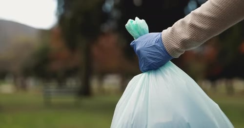 Park, person and hand with garbage bag in nature for environment, cleaning and community service