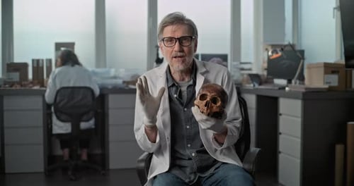 Mature Lab Worker or Scientist Shows Fossil Skull of Ancient Human for Documentary Film