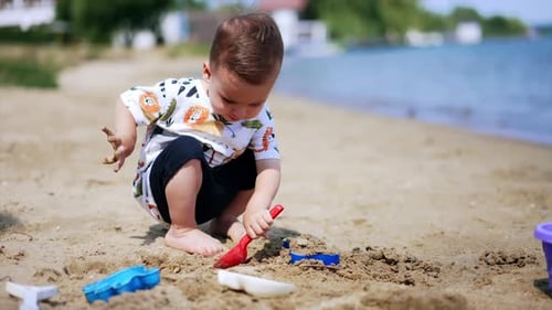 Kid is playing with toys on the beach on sunny day. Baby digs the ground with a shovel.