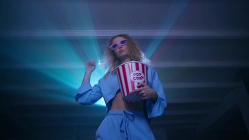 Femme heureuse dansant en mangeant du pop-corn en regardant un concert sur un projecteur à la maison