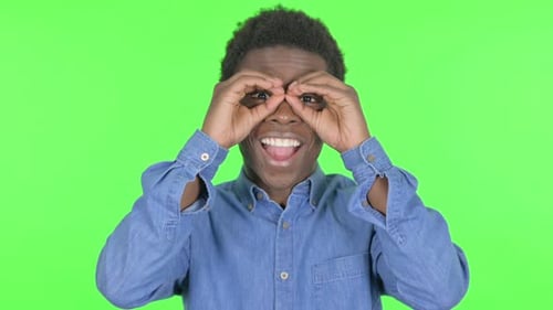 Junger Afrikaner schaut sich mit handgemachtem Fernglas auf grünem Hintergrund um